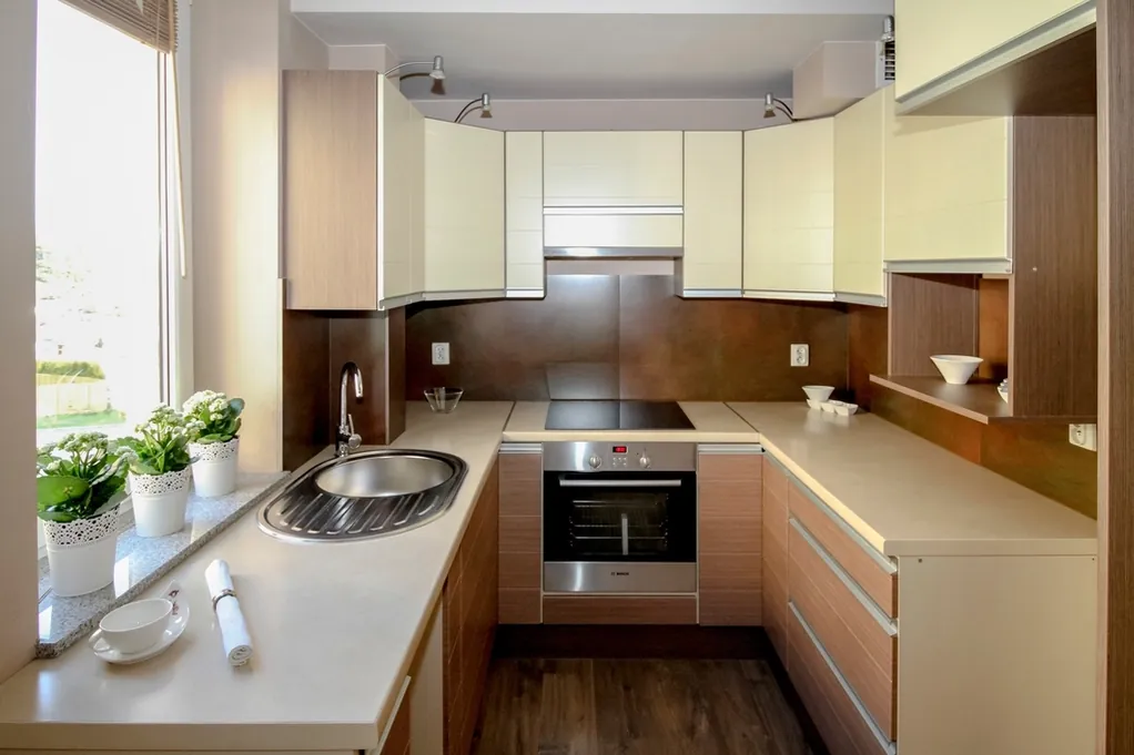 Después: cocina en U con muebles claros, encimera de cuarzo y horno en columna
