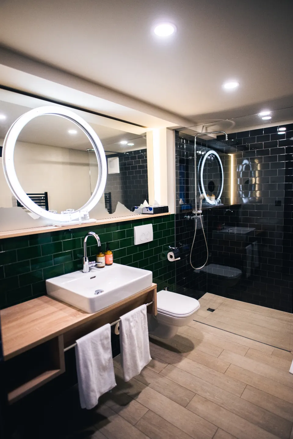 Baño reformado con azulejo verde, lavabo sobre mueble de madera y espejo redondo